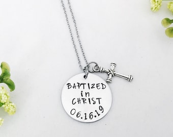Puede incluir: Collar de plata con un colgante redondo que dice "Bautizado en Cristo 06.16.19" y un pequeño dije de cruz de plata.
