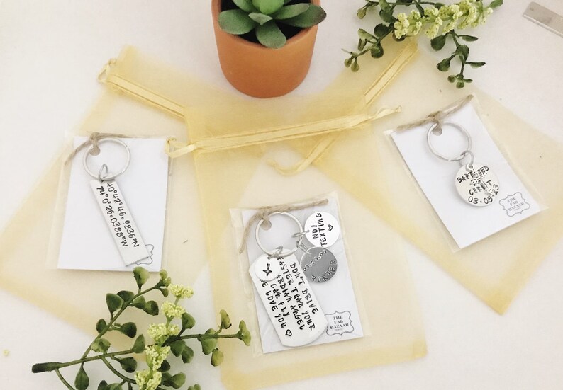 May include: Three small gift bags containing keychains. The keychains are made of metal and feature different sayings. The bags are made of a sheer, gold material.