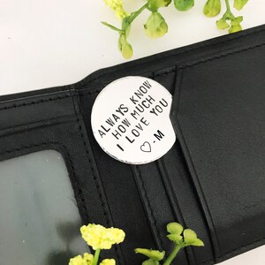 May include: A black leather wallet with a silver charm attached. The charm has the text "Always know how much I love you -M" on it.