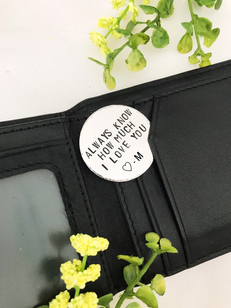 May include: A black leather wallet with a silver charm attached. The charm has the text "Always know how much I love you -M" on it.