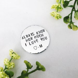 May include: A silver metal disc with the text "ALWAYS KNOW HOW MUCH I LOVE YOU -M" and a small heart symbol.