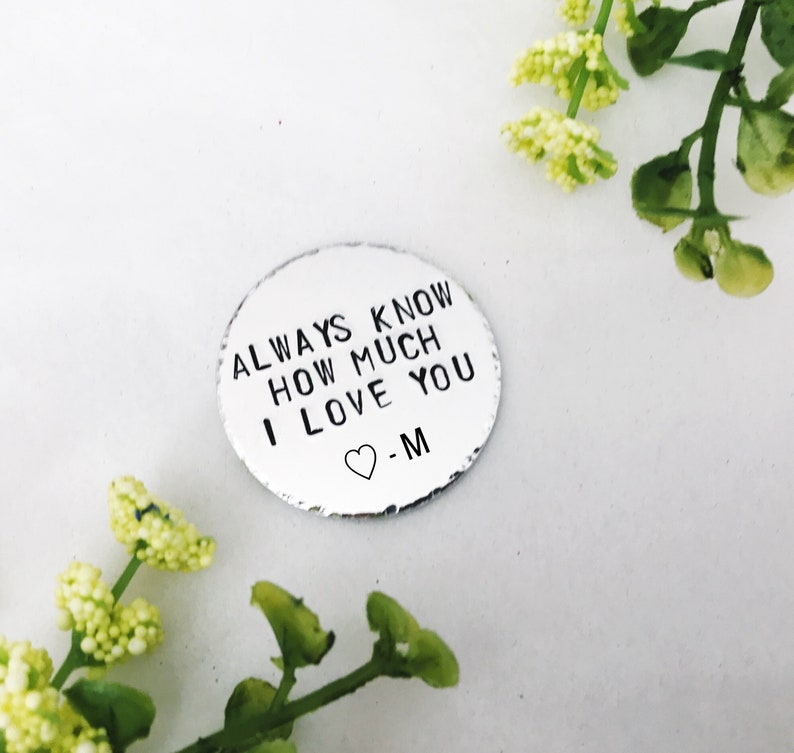 May include: A silver metal disc with the text "ALWAYS KNOW HOW MUCH I LOVE YOU -M" and a small heart symbol.