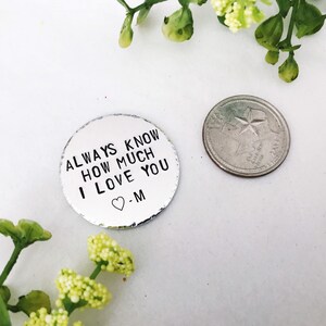 May include: A silver metal disc with the text "ALWAYS KNOW HOW MUCH I LOVE YOU" and a heart symbol followed by the letter "M". The disc is about the size of a UK 20 pence coin.