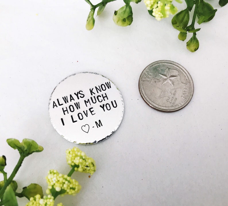 May include: A silver metal disc with the text "ALWAYS KNOW HOW MUCH I LOVE YOU" and a heart symbol followed by the letter "M". The disc is about the size of a UK 20 pence coin.