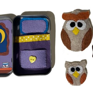 May include: A small tin box with a felt bed inside. The box is open and shows a felt bed with a yellow button and a heart shape. There are two felt owls and a felt butterfly outside the box.