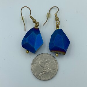 Peut inclure: Une paire de boucles d'oreilles en pierre bleue avec du fil d'or enroul&eacute; autour du sommet de la pierre et des crochets dor&eacute;s. Les boucles d'oreilles sont &agrave; peu pr&egrave;s de la taille d'une pi&egrave;ce de 25 cents am&eacute;ricaine.