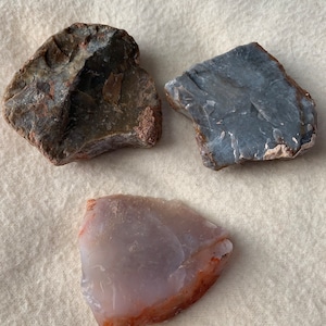 以下が含まれることがあります： 不規則な形の瑪瑙が3つあり、1つはグレー、1つは茶色と白、もう1つは赤みがかった縁のある薄いパープルです。