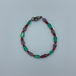 May include: A bracelet made of green, purple, and red glass beads. The beads are shaped like tulips.