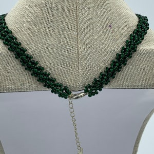 May include: A green beaded necklace with a silver clasp and extender chain. The necklace is on a white mannequin.