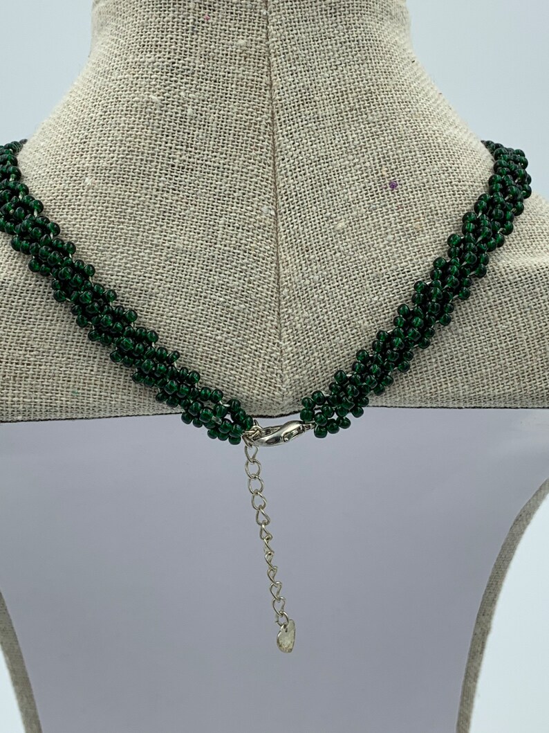 May include: A green beaded necklace with a silver clasp and extender chain. The necklace is on a white mannequin.
