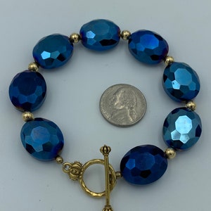 May include: A blue crystal bead bracelet with a gold toggle clasp. The beads are faceted and have a metallic sheen.
