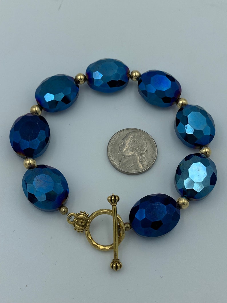 May include: A blue crystal bead bracelet with a gold toggle clasp. The beads are faceted and have a metallic sheen.