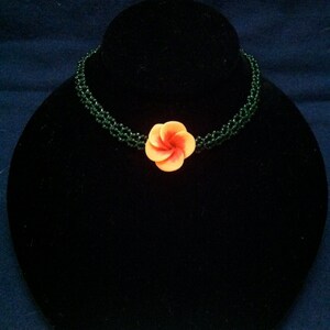 May include: A green beaded choker necklace with a single orange and pink flower charm.