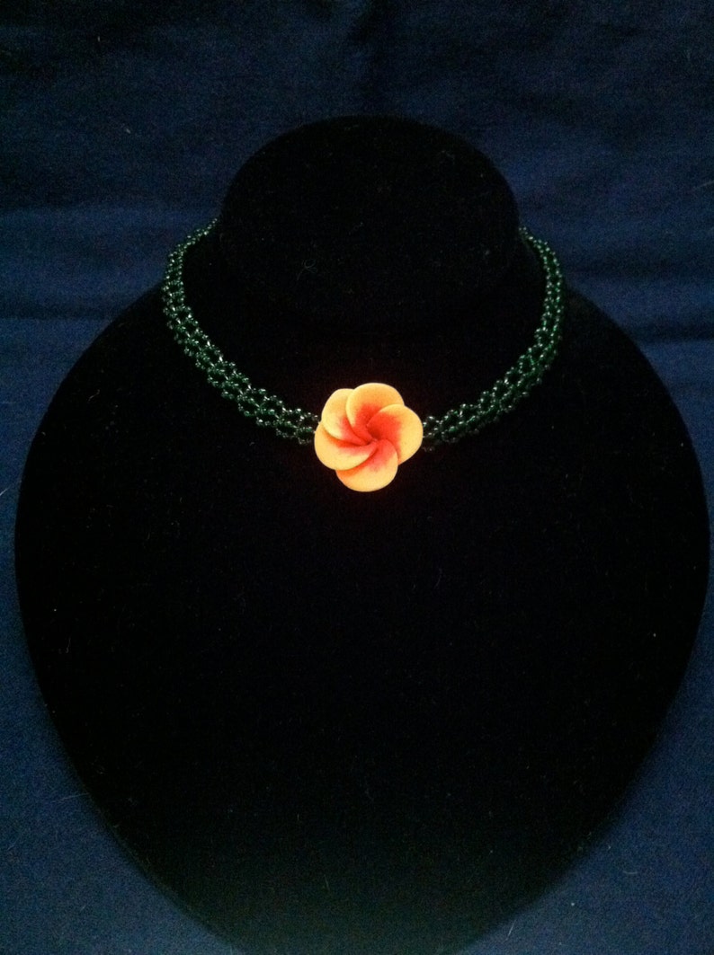 May include: A green beaded choker necklace with a single orange and pink flower charm.