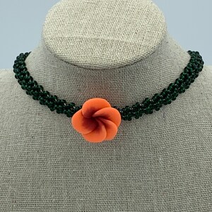 May include: A green beaded choker necklace with a coral-colored flower charm.