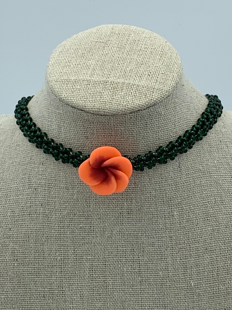 May include: A green beaded choker necklace with a coral-colored flower charm.