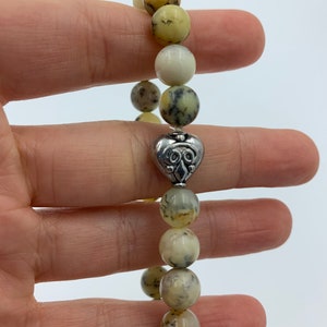 May include: A bracelet made of light brown and white stones with a silver heart charm.