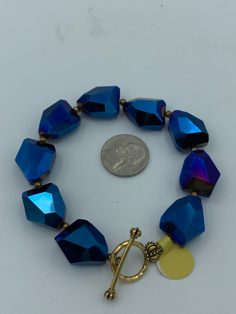 Peut inclure: Un bracelet en cristal bleu avec un fermoir et un charme en or. Le bracelet est compos&eacute; de cristaux facet&eacute;s iris&eacute;s.
