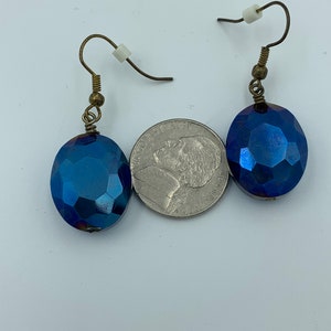 May include: A pair of blue iridescent glass earrings with gold-toned hooks. The earrings are oval shaped and have a faceted design.
