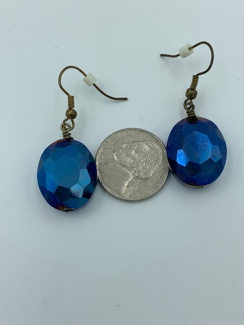 May include: A pair of blue iridescent glass earrings with gold-toned hooks. The earrings are oval shaped and have a faceted design.