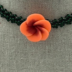 May include: A multi-strand necklace made of dark green beads with a coral-colored flower pendant.