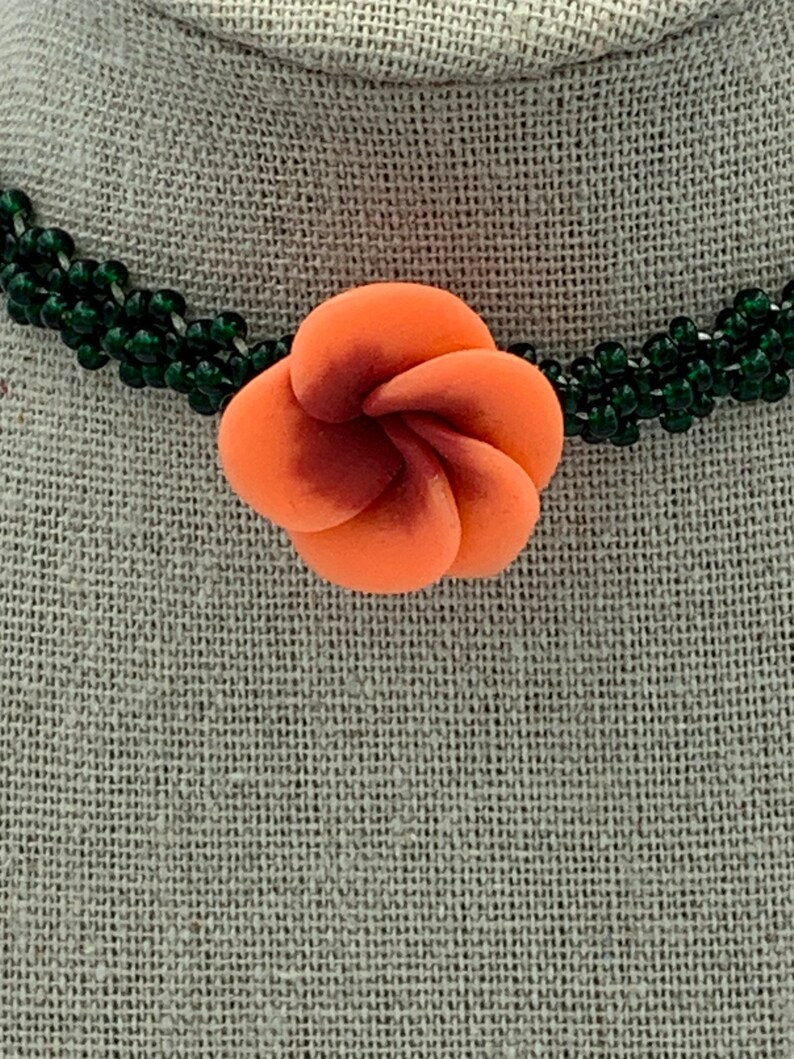 May include: A multi-strand necklace made of dark green beads with a coral-colored flower pendant.