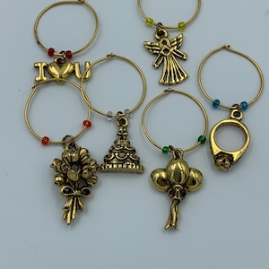 May include: Set of six gold-tone wine glass charms with different charms, including an angel, a ring, a cake, balloons, a bouquet of flowers, and an "I love you" charm.