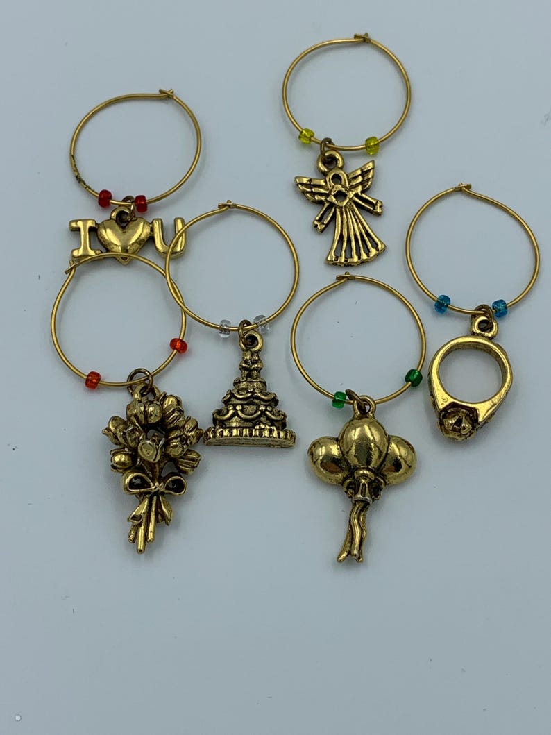 May include: Set of six gold-tone wine glass charms with different charms, including an angel, a ring, a cake, balloons, a bouquet of flowers, and an "I love you" charm.