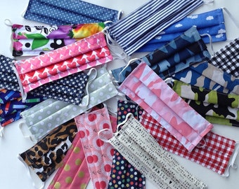 May include: A collection of colorful fabric face masks with various patterns, including polka dots, hearts, stars, and floral designs. Some masks have text printed on them, including "Love find your home" and "Family there's no place like home".