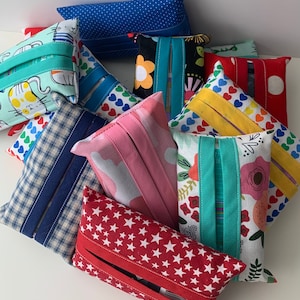May include: A collection of nine colorful fabric tissue box covers. The covers feature various patterns, including polka dots, hearts, stars, and floral designs. Each cover has a slot for pulling out tissues.