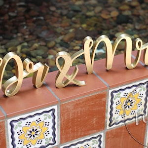 May include: Gold wooden letters spelling "Mr & Mrs" on a tiled surface.