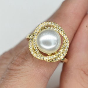 May include: A gold ring featuring a large white pearl encircled by a double row of sparkling clear stones.