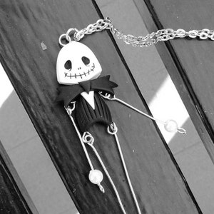May include: A black and white polymer clay pendant necklace featuring a Jack Skellington character from the movie 'The Nightmare Before Christmas'. The pendant is attached to a silver chain with white pearl accents.