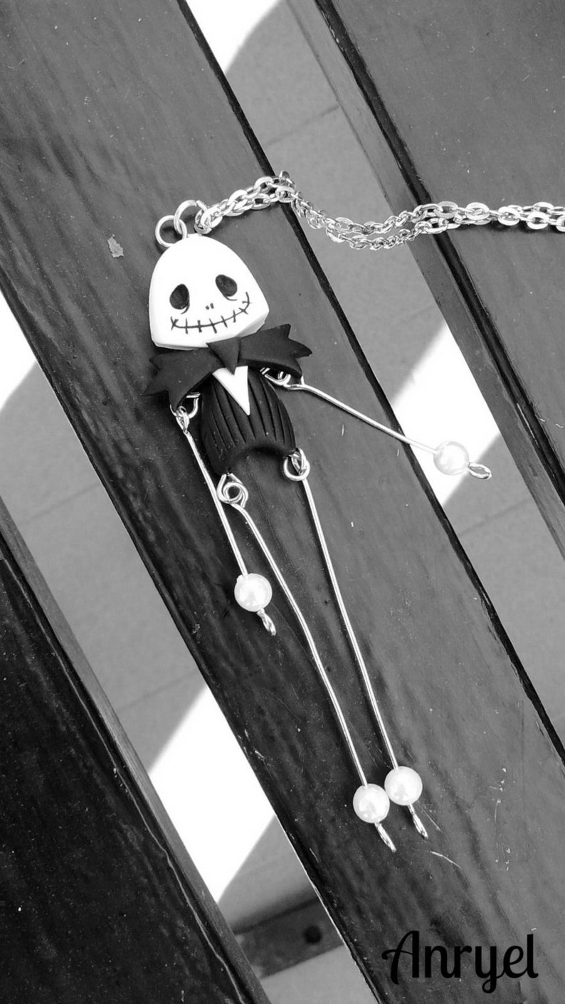 May include: A black and white polymer clay pendant necklace featuring a Jack Skellington character from the movie 'The Nightmare Before Christmas'. The pendant is attached to a silver chain with white pearl accents.