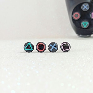 Puede incluir: Cuatro botones redondos negros con diferentes símbolos de colores, que representan los botones del mando de PlayStation: triángulo, círculo, cruz y cuadrado.