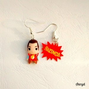 May include: A pair of earrings featuring a cartoon character with brown hair and a red shirt with the word "Bazinga!" on a red starburst.