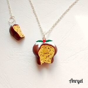 May include: A silver chain necklace with a Christmas pudding charm. The charm is made of polymer clay and is painted to look like a traditional Christmas pudding with a white icing topping, red holly berry, and green leaves. The charm is split open to show the inside of the pudding.