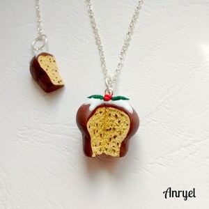 May include: A silver chain necklace with a pendant of a chocolate-covered Christmas pudding with a sprig of holly on top. The pendant is split in half to show the inside of the pudding. A smaller version of the pendant is also included on a separate chain.