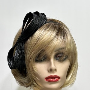 May include: A black headband with a woven bow detail. The bow is made of a textured material and is attached to a thin black band. The headband is worn on a mannequin with blonde hair and red lipstick.