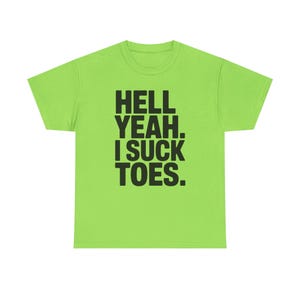 May include: A lime green t-shirt featuring the phrase "HELL YEAH. I SUCK TOES." in bold black capital letters. The t-shirt has a crew neck and is likely made from a comfortable fabric.