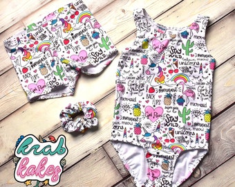 Könnte beinhalten: Weißer Tanzanzug und passende Shorts mit einem bunten Druck mit Einhörnern, Ananas, Flamingos und dem Text "Stay Wild" und "Girl Power".
