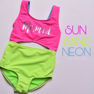 May include: A neon green and pink swimsuit with a cutout in the middle. The top of the swimsuit has a silver glitter "Mermaid" design. The text "SUN SAND NEON" is written in pink, yellow, and blue letters on the right side of the image. The text "Krab Kokes 2019" is written in blue letters below the text "NEON".
