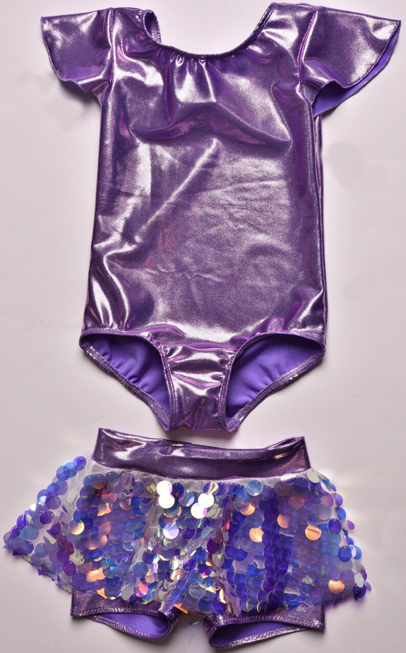 May include: A purple leotard with short, ruffled sleeves and a matching sequined skirt. The skirt has a white lining and iridescent sequins.