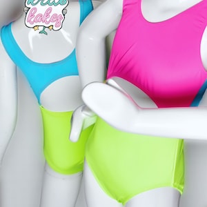 May include: Two mannequins wearing bright neon leotards. The leotard on the left is turquoise and lime green. The leotard on the right is hot pink and lime green.