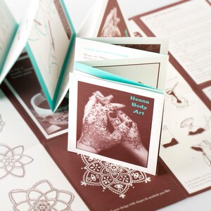 May include: A folded paper booklet with a brown cover and a teal blue spine. The cover features a close-up image of henna body art on two hands. The text on the cover reads "Henna Body Art".