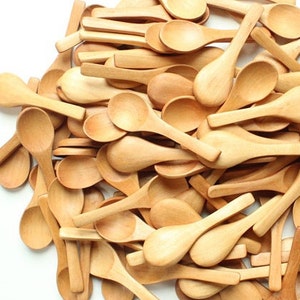 May include: A pile of small, wooden spoons. The spoons are all natural wood color and are arranged in a random pattern.
