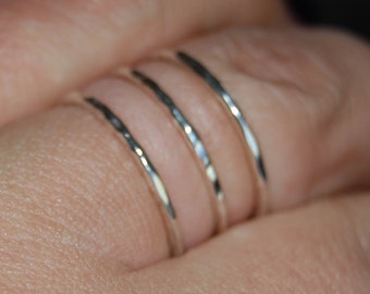 May include: Four silver stacking rings on a finger. The rings are thin and have a hammered texture.