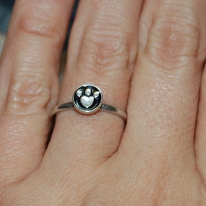 Op de afbeelding: Een zilveren ring met een zwart-witte pootprint.