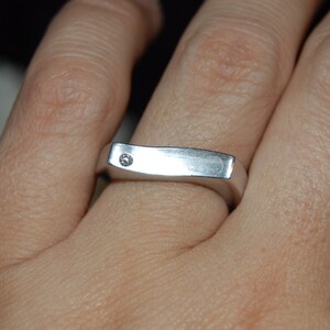 May include: A silver band ring with a single small diamond set into the top of the band.