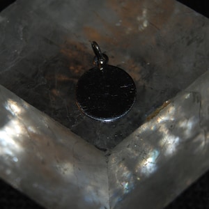 May include: A silver charm with a round, smooth surface. The charm is hanging from a loop at the top.